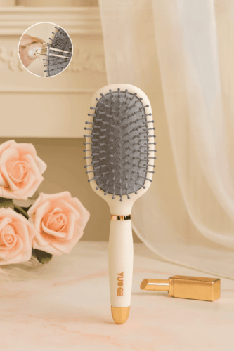 Brosse à cheveux antistatique à coussin d’air couleur beige avec picots souples, posée sur une table avec roses et rouge à lèvres doré